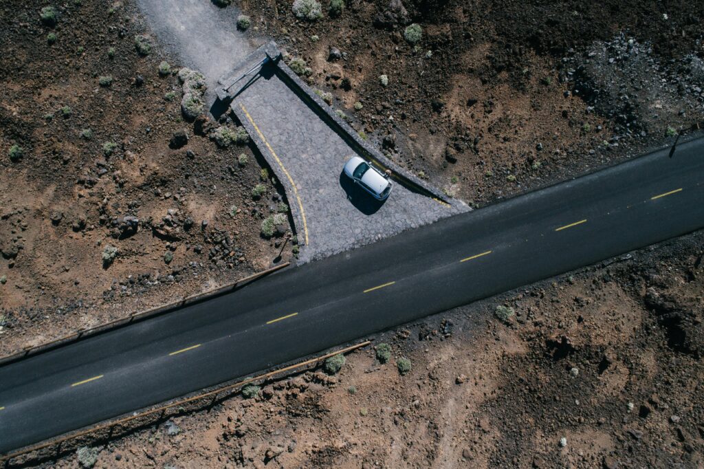 An aerial view of a solitary car parked alongside a deserted road in a barren landscape.